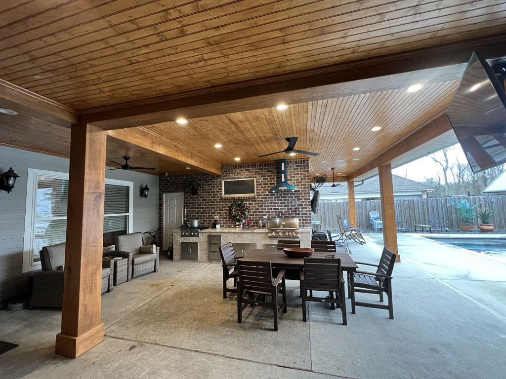 A covered patio with a wood ceiling and a table and chairs.